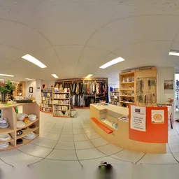 Overzicht van kringloopwinkel met kledingrekken, boekenkasten, servies en huishoudartikelen uitgestald