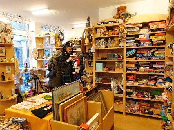 Winkelvloer met houten stellingen vol boeken, speelgoed, beeldjes en diversen spullen, klant aan het kijken