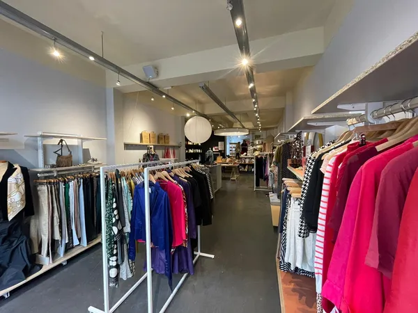 Winkelinterieur met kledingrekken vol dameskleding in verschillende kleuren, onder meer felroze items aan rechterkant, verlic