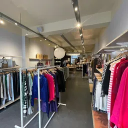 Winkelinterieur met kledingrekken vol dameskleding in verschillende kleuren, onder meer felroze items aan rechterkant, verlic