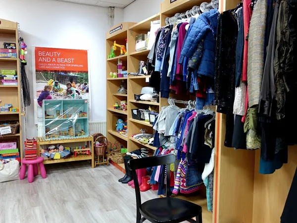 Winkelvloer met houten stellingen vol kinderkledinhaangers, speelgoed en boeken