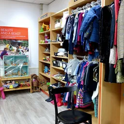 Winkelvloer met houten stellingen vol kinderkledinhaangers, speelgoed en boeken