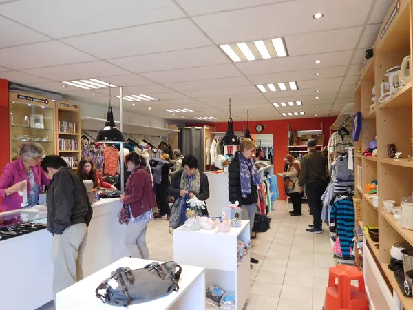 Winkelvloer met bezoekers, stellingen met kleding en accessoires, witte display tafels en rode accenten