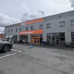 Gevel van kringloopwinkel Azalee met oranje uithangbord, ingang met glazen deuren en fietsen ernaast