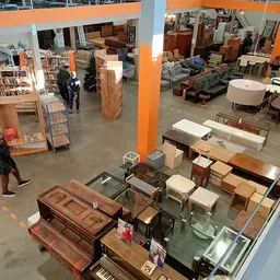Overzicht van een kringloopwinkel met meubels, tafels, stoelen en huishoudspullen uitgestald op de vloer