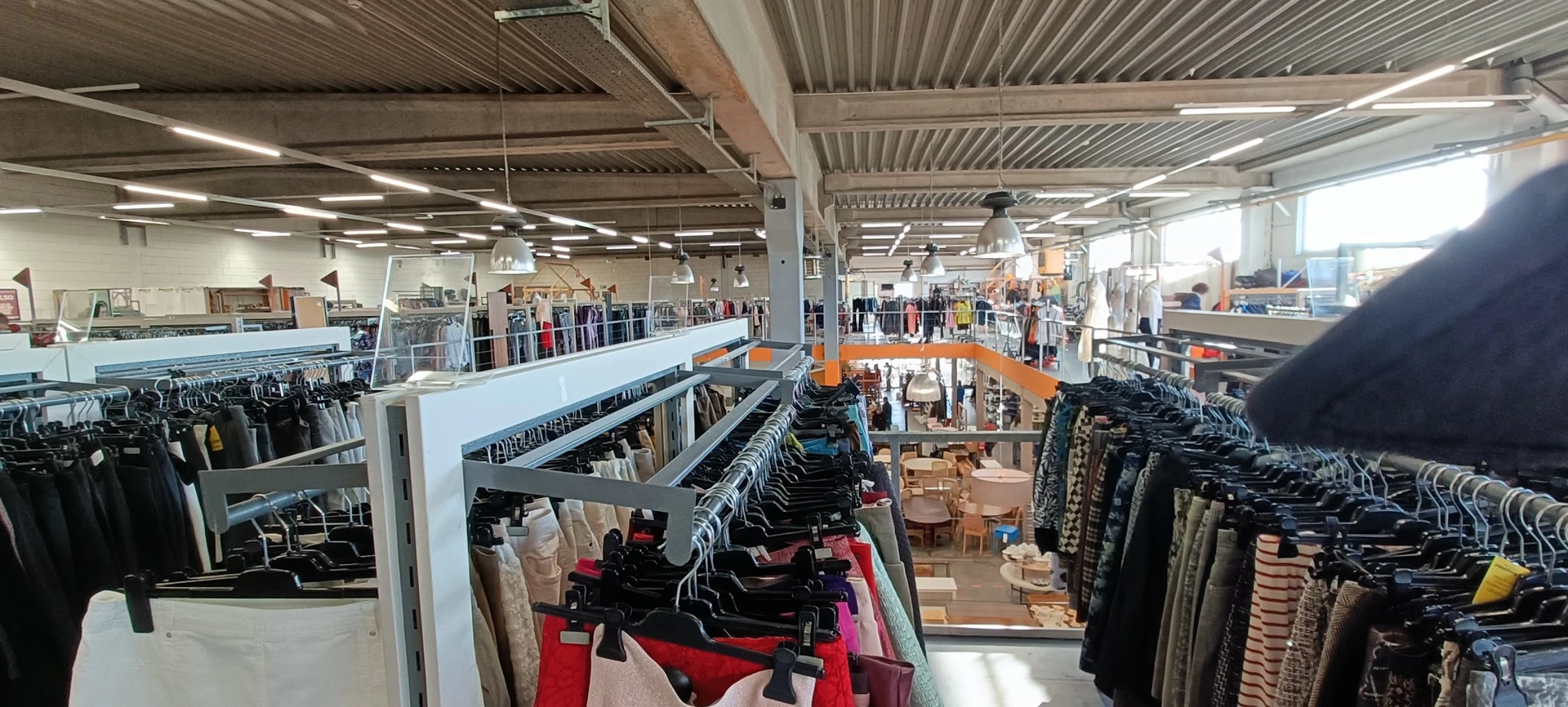 Overzicht van tweedehands kledingwinkel met rekken vol kleding, stellingen en verlichte zolderruimte