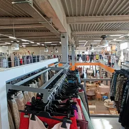 Overzicht van tweedehands kledingwinkel met rekken vol kleding, stellingen en verlichte zolderruimte