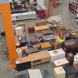 Diverse tweedehands meubels uitgestald op een winkelvoer, waaronder tafels, kasten en kleinere meubelstukken met roze prijska