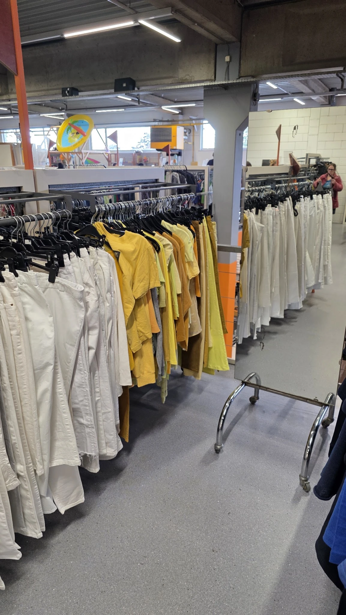Rekken met tweedehands kleding in verschillende kleuren: wit, geel, oranje en groen.