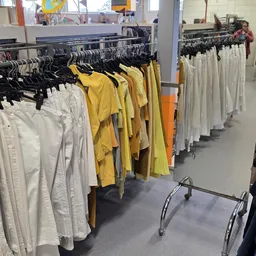 Rekken met tweedehands kleding in verschillende kleuren: wit, geel, oranje en groen.