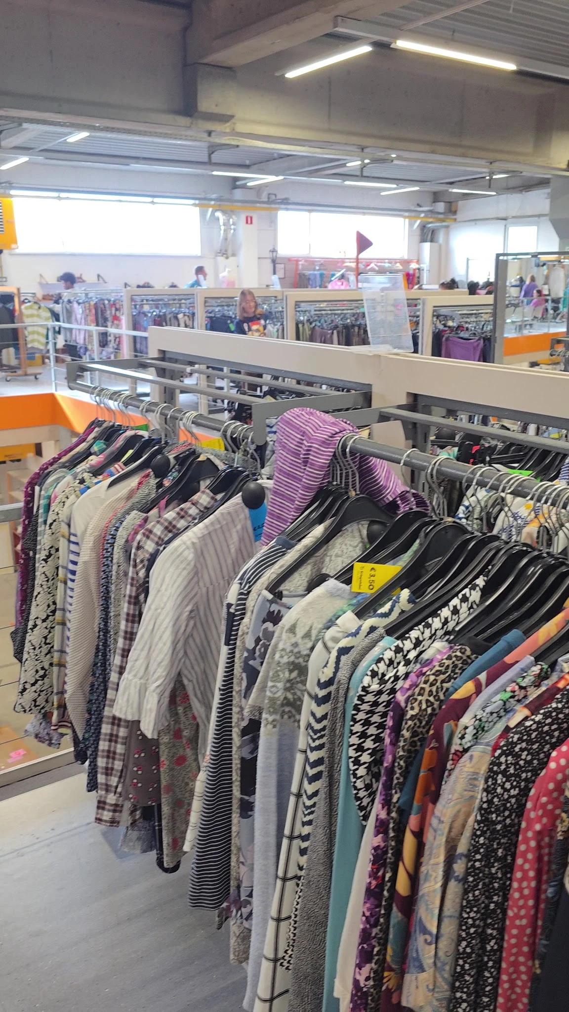 Rekken met tweedehands kleding op hangers, waaronder gestreepte en gedessineerde items in verschillende kleuren