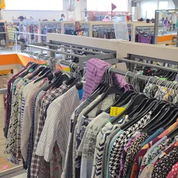 Rekken met tweedehands kleding op hangers, waaronder gestreepte en gedessineerde items in verschillende kleuren