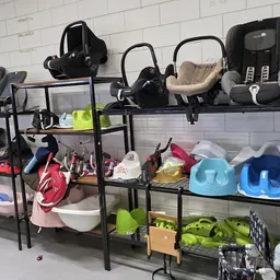 Zwart stellingkast systeem met tweedehands babyartikelen: autostoeltjes, kinderstoelen, helmen en speelgoed netjes uitgestald