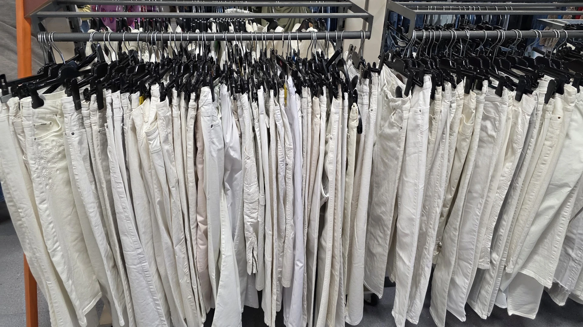 Rekken met witte kleding op hangers, waaronder broeken en andere kledingstukken in verschillende maten