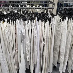 Rekken met witte kleding op hangers, waaronder broeken en andere kledingstukken in verschillende maten