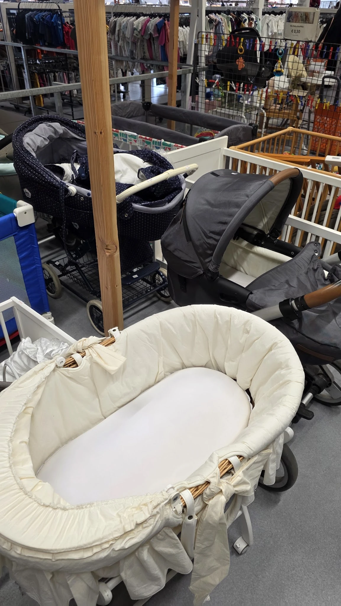Witte babywieg met houten stijl in kringloopwinkel, omgeven door kinderwagens