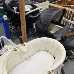 Witte babywieg met houten stijl in kringloopwinkel, omgeven door kinderwagens