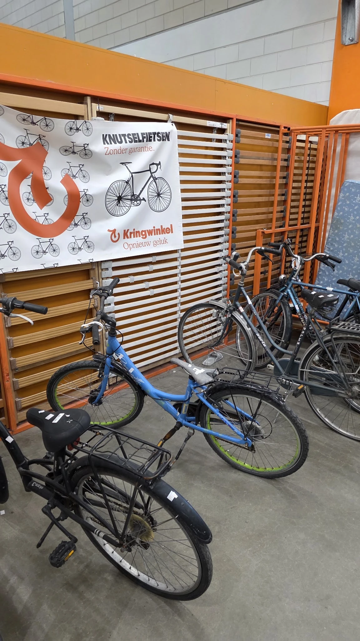 Uitgestalde tweedehandsfietsenen fietsen in een kringloopwinkel met houten stellingen op de achtergrond