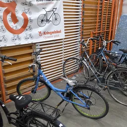Uitgestalde tweedehandsfietsenen fietsen in een kringloopwinkel met houten stellingen op de achtergrond