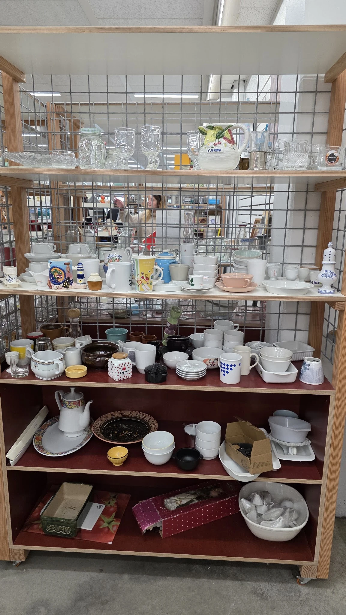 Glazen vitrine met diverse tweedehands serviesgoed, kopjes, kannen en potten