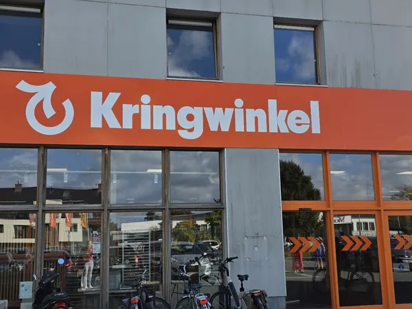 Winkelgevel met oranje Kringwinkel-logo en grote ramen, fietsen geparkeerd ervoor