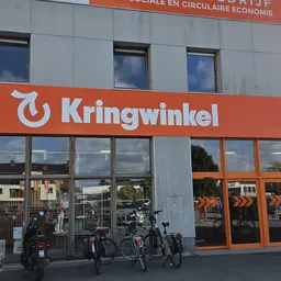 Winkelgevel met oranje Kringwinkel-logo en grote ramen, fietsen geparkeerd ervoor