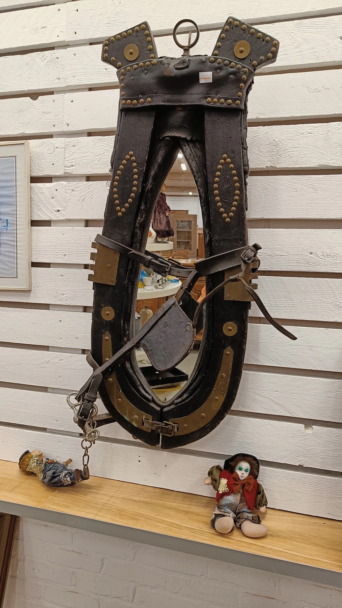 Antieke zwarte lederen paardentuig met bronzen details, opgehangen aan houten wand