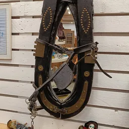 Antieke zwarte lederen paardentuig met bronzen details, opgehangen aan houten wand