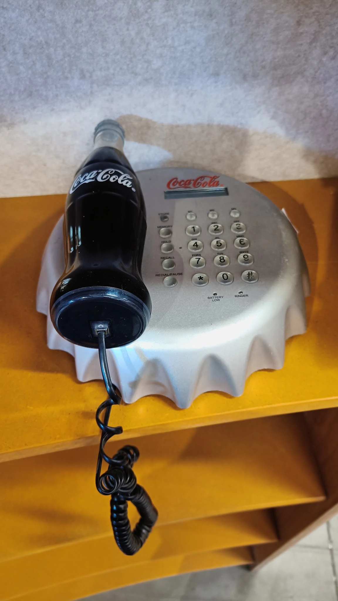 Vintage Coca-Cola telefoon met nummertoetsen op witte basis met geel tafelblad