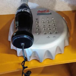 Vintage Coca-Cola telefoon met nummertoetsen op witte basis met geel tafelblad
