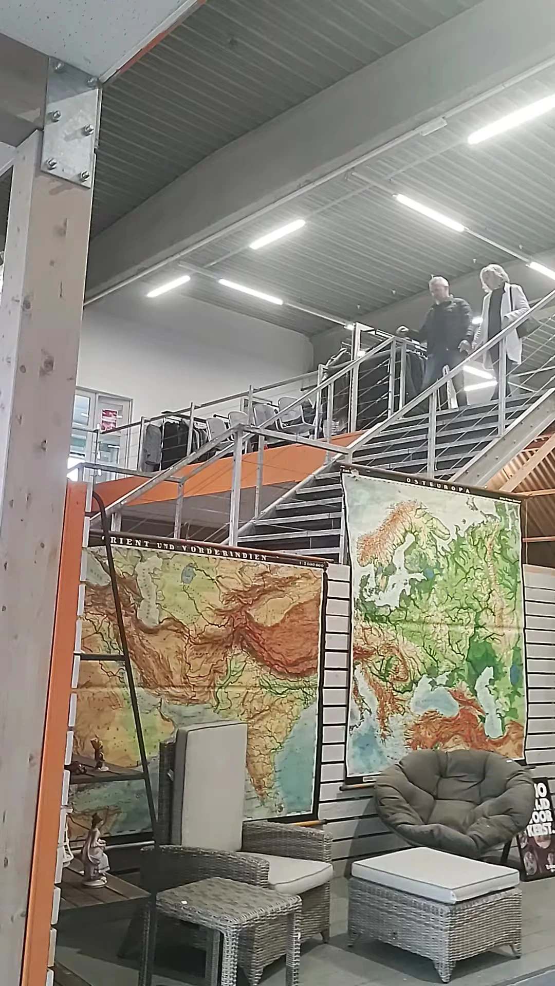 Winkelinterieur met stalen stellingen, trappen en geograafische kaarten tegen de wand