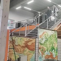 Winkelinterieur met stalen stellingen, trappen en geograafische kaarten tegen de wand