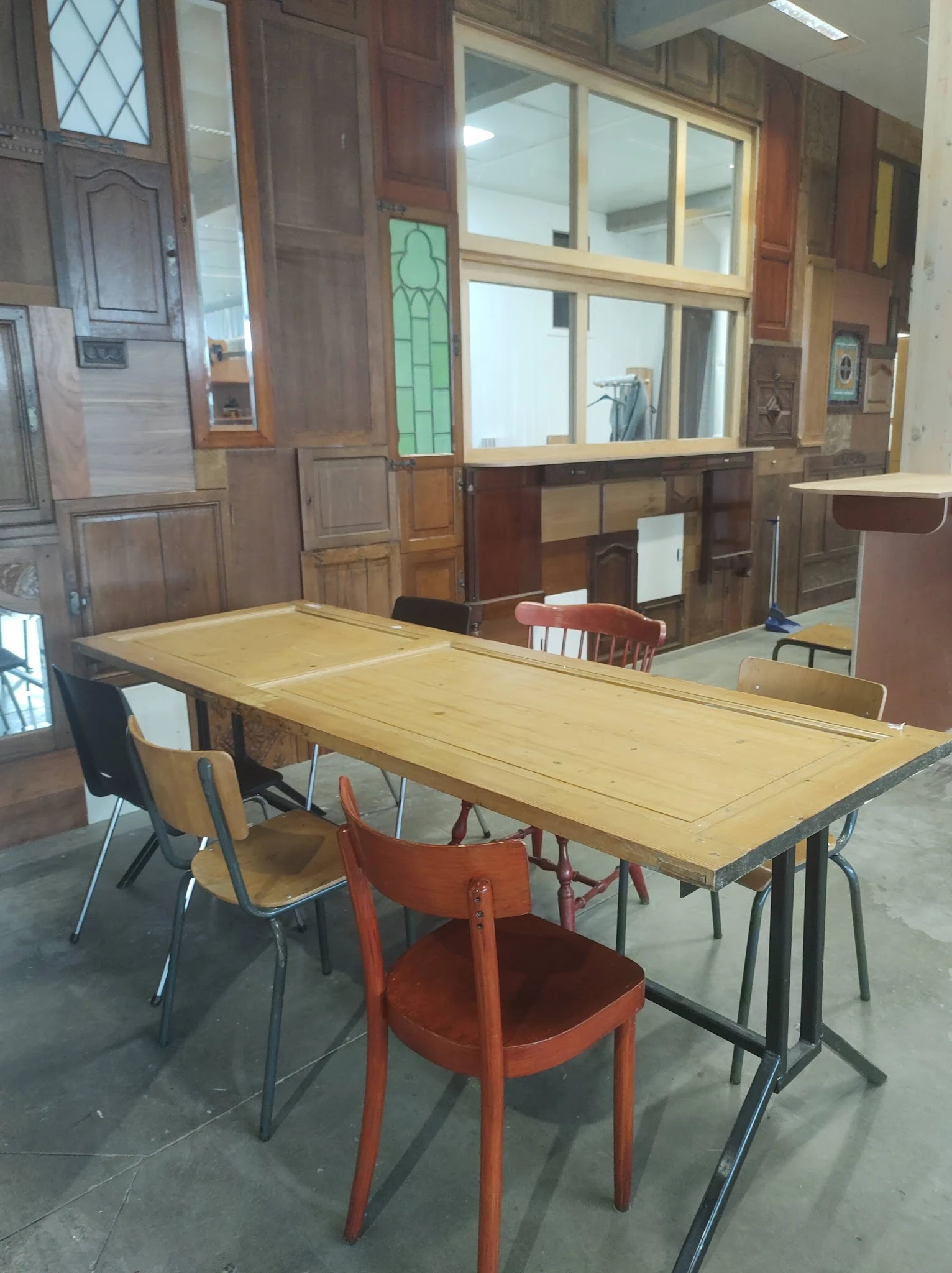 Winkelvloer met lange houten tafel, diverse stoelen en houten kasten op de achtergrond