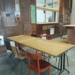 Winkelvloer met lange houten tafel, diverse stoelen en houten kasten op de achtergrond