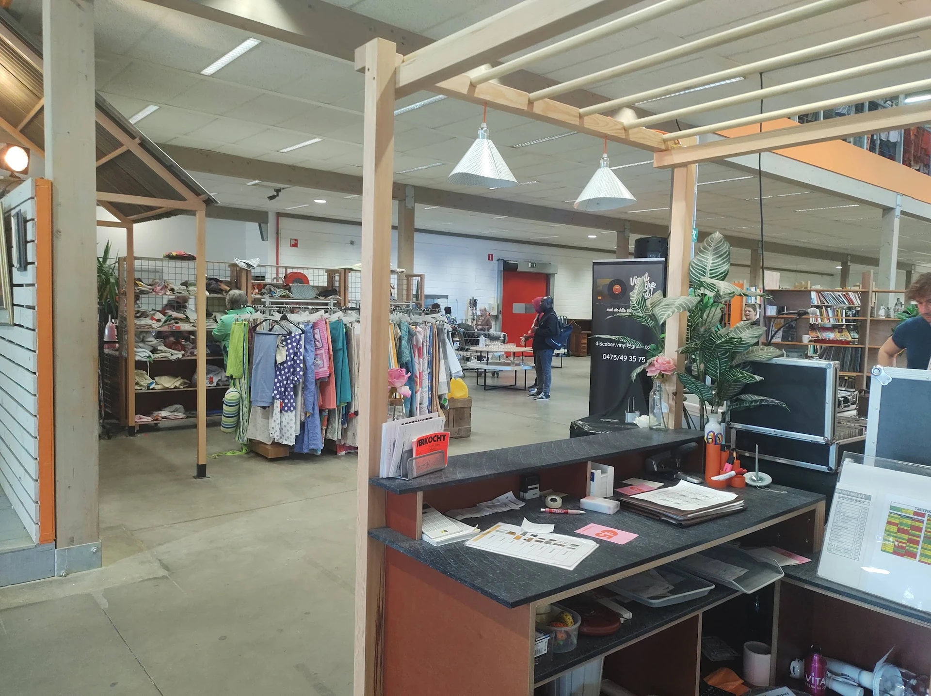 Winkelvloer met kledingrekken, boekenkasten en een balie met computerscherm in een kringloopwinkel