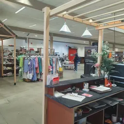Winkelvloer met kledingrekken, boekenkasten en een balie met computerscherm in een kringloopwinkel