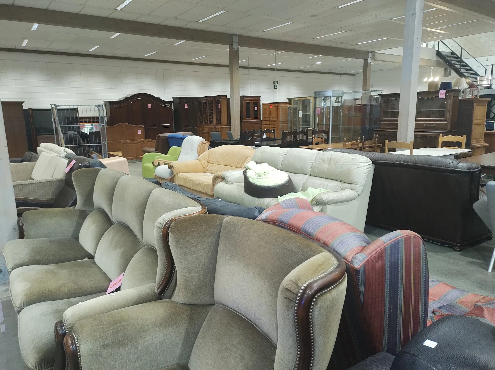 Uitgestalde fauteuils en meubels in een kringloopwinkel, met in de achtergrond kasten en andere meubelstukken