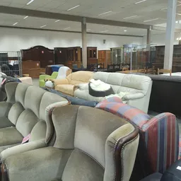 Uitgestalde fauteuils en meubels in een kringloopwinkel, met in de achtergrond kasten en andere meubelstukken