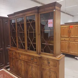 Houten meubels met glazen deuren en kasten in kringloopwinkel, waaronder een vitrinekast met ruitpatroon