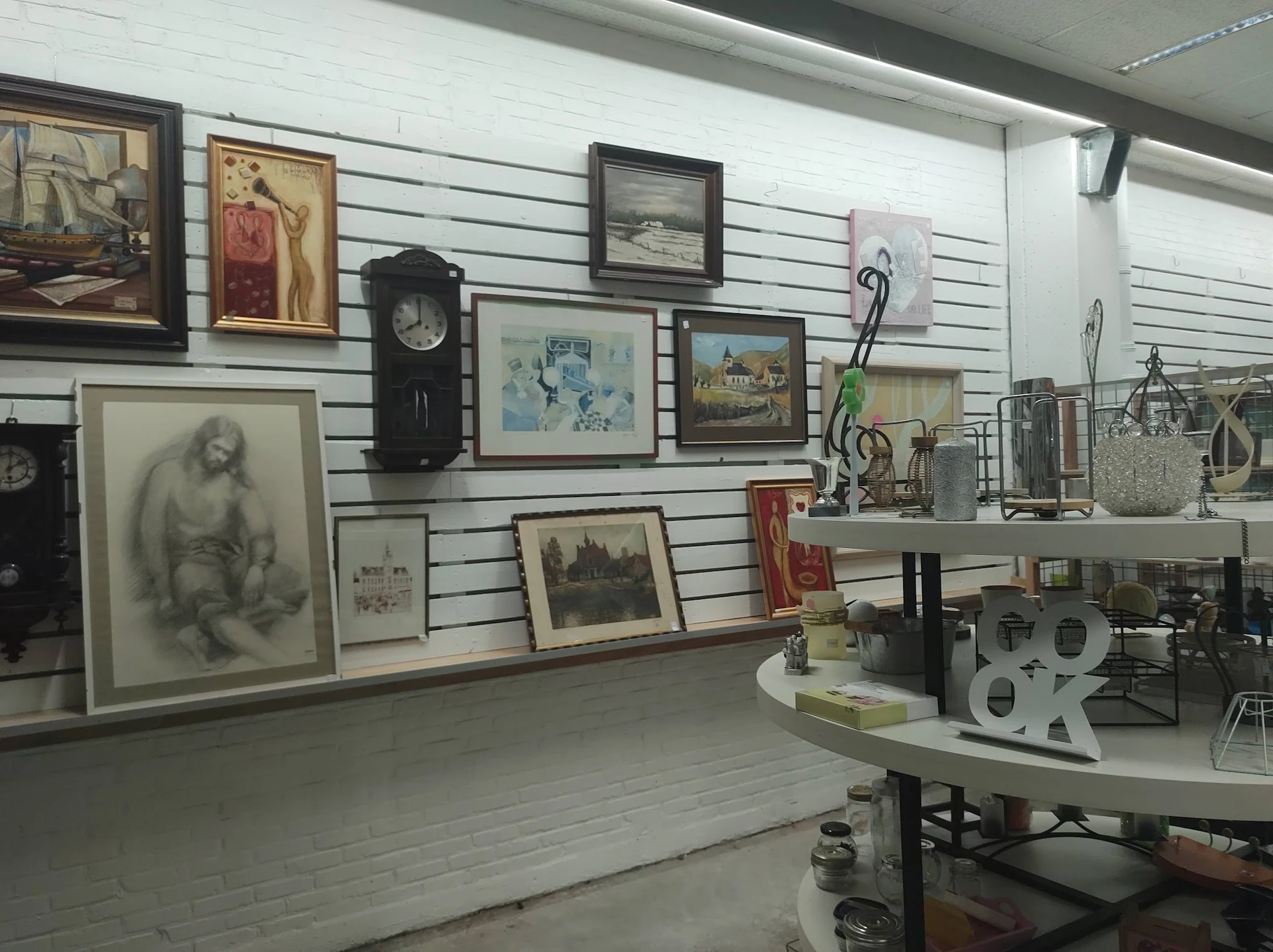 Winkelvloer met slatwall waaraan diverse tweedehands kunstwerken, schilderijen, klokken en decoratieartikelen zijn uitgestald