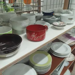 Uitgestalde serviesgoed en schalen in verschillende kleuren op een witte tafel in de winkel