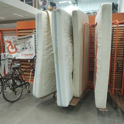Matrassen en bedbodem uitgestald in de winkel, naast een fiets en oranje stellingen