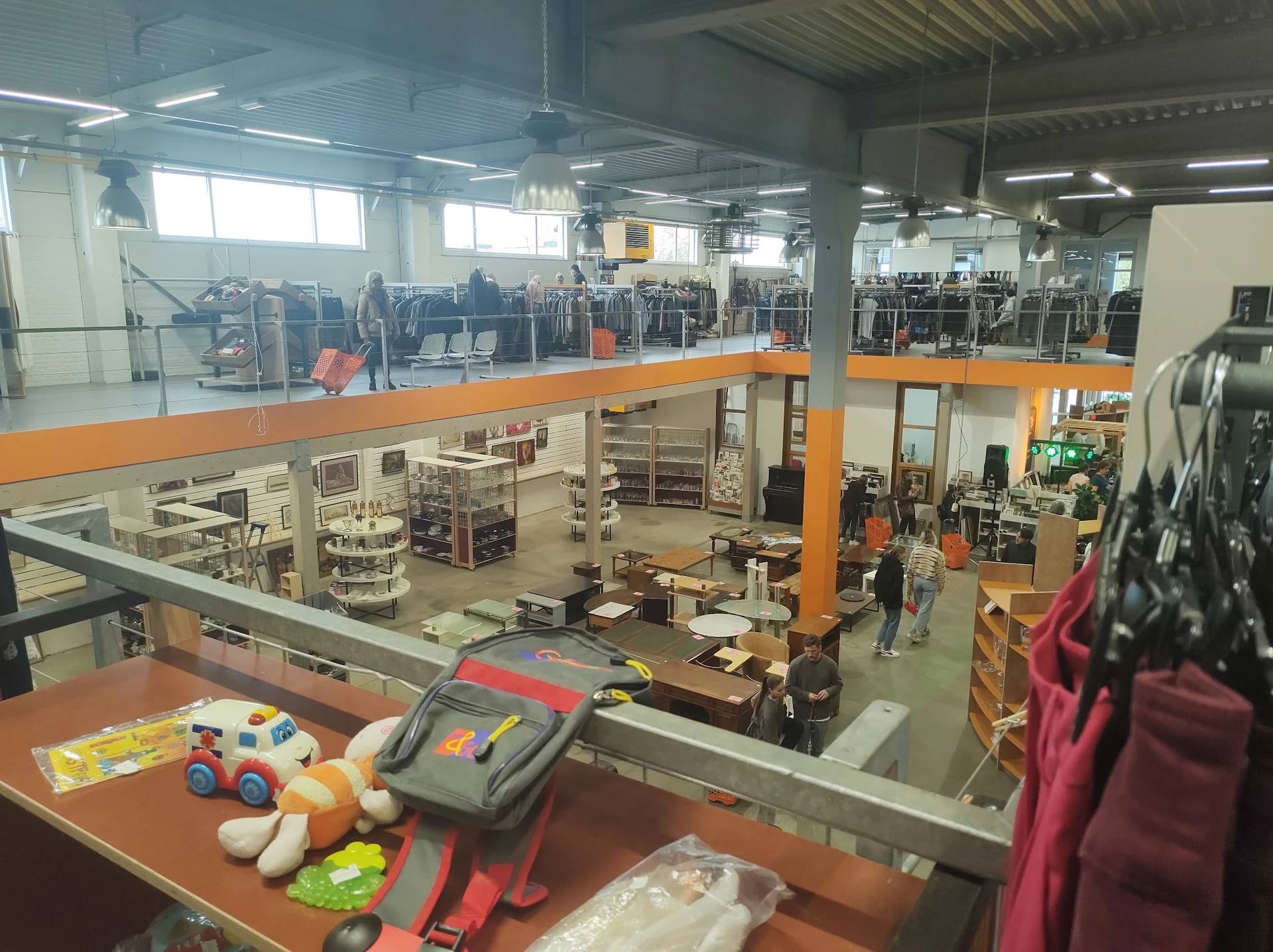 Overzicht van kringloopwinkel met twee verdiepingen, stellingen met spullen en speelgoed op voorgrond