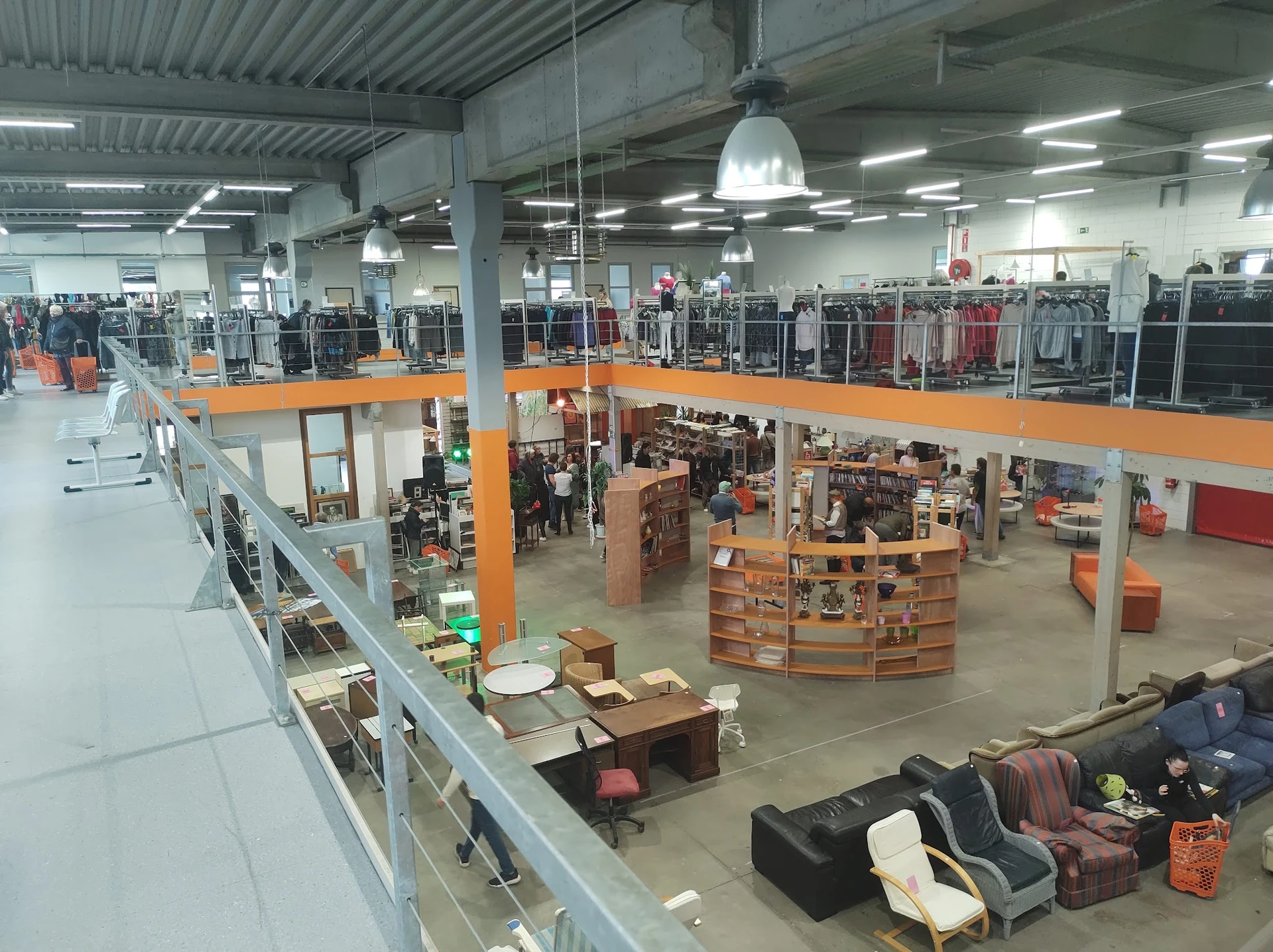 Overzicht van kringloopwinkel met twee verdiepingen, oranje balkons, stellingen met kleding en diversen spullen