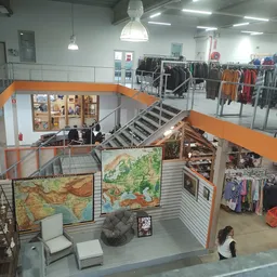 Overzicht van tweedehands winkel met oranje accenten, rekken met kleding op beide verdiepingen en themagebieden met decoratie