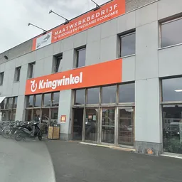 Gevel van kringloopwinkel met oranje Kringwinkel-logo en ingang, fietsen geparkeerd ervoor