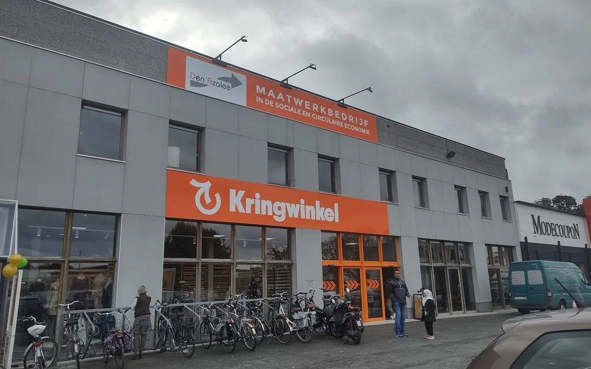 Gevel van kringloopwinkel met oranje banden, winkelnaam Kringwinkel, fietsenstalling ervoor