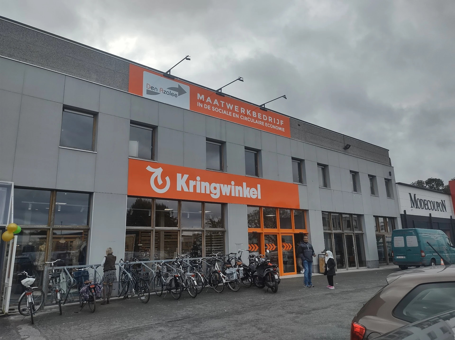 Gevel van kringloopwinkel met oranje banden, winkelnaam Kringwinkel, fietsenstalling ervoor