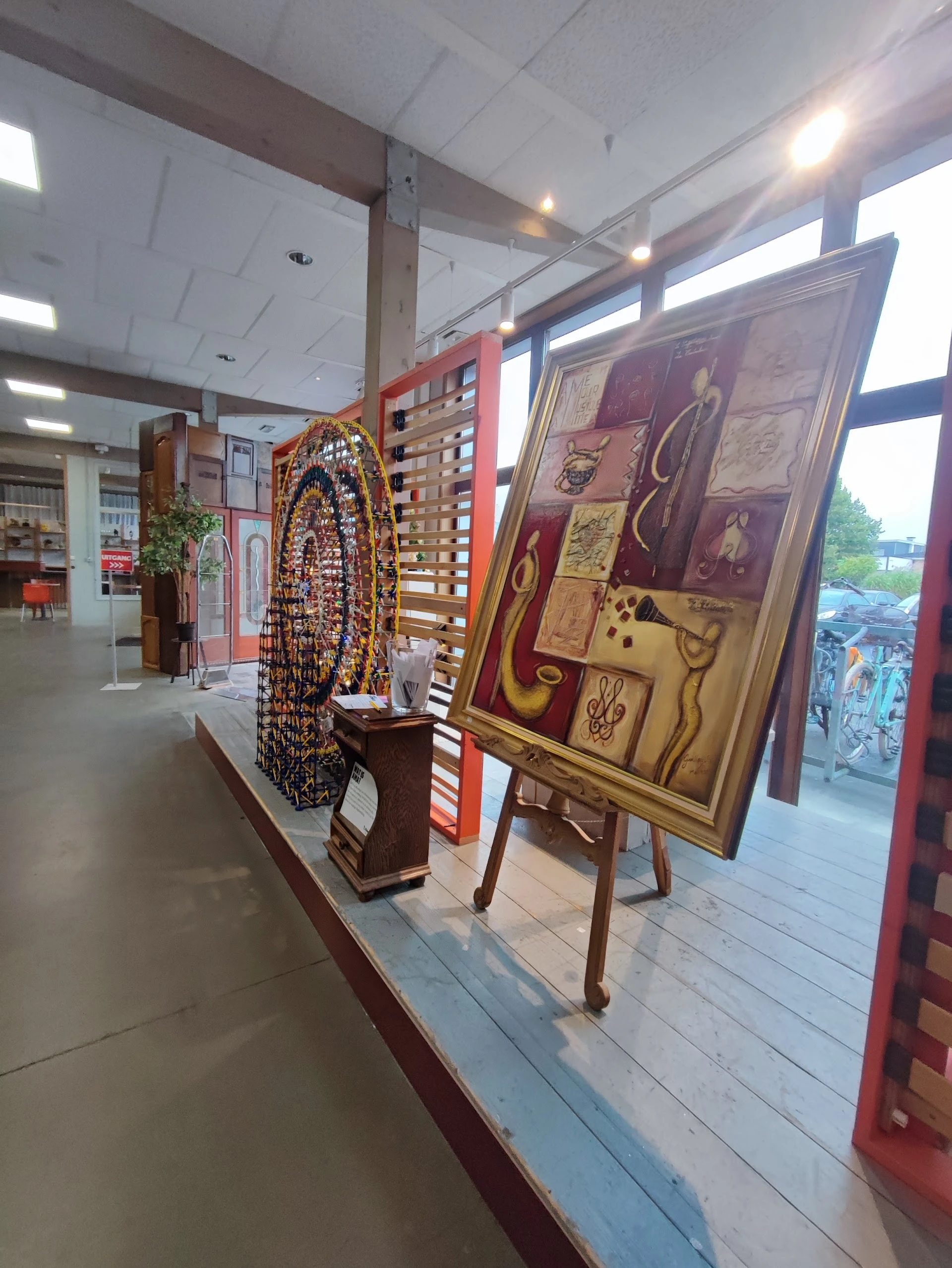 Uitgestalde kunstobjecten en decoratieve items in de winkel, waaronder een beeldhouwwerk en schilderijen op houten panelen
