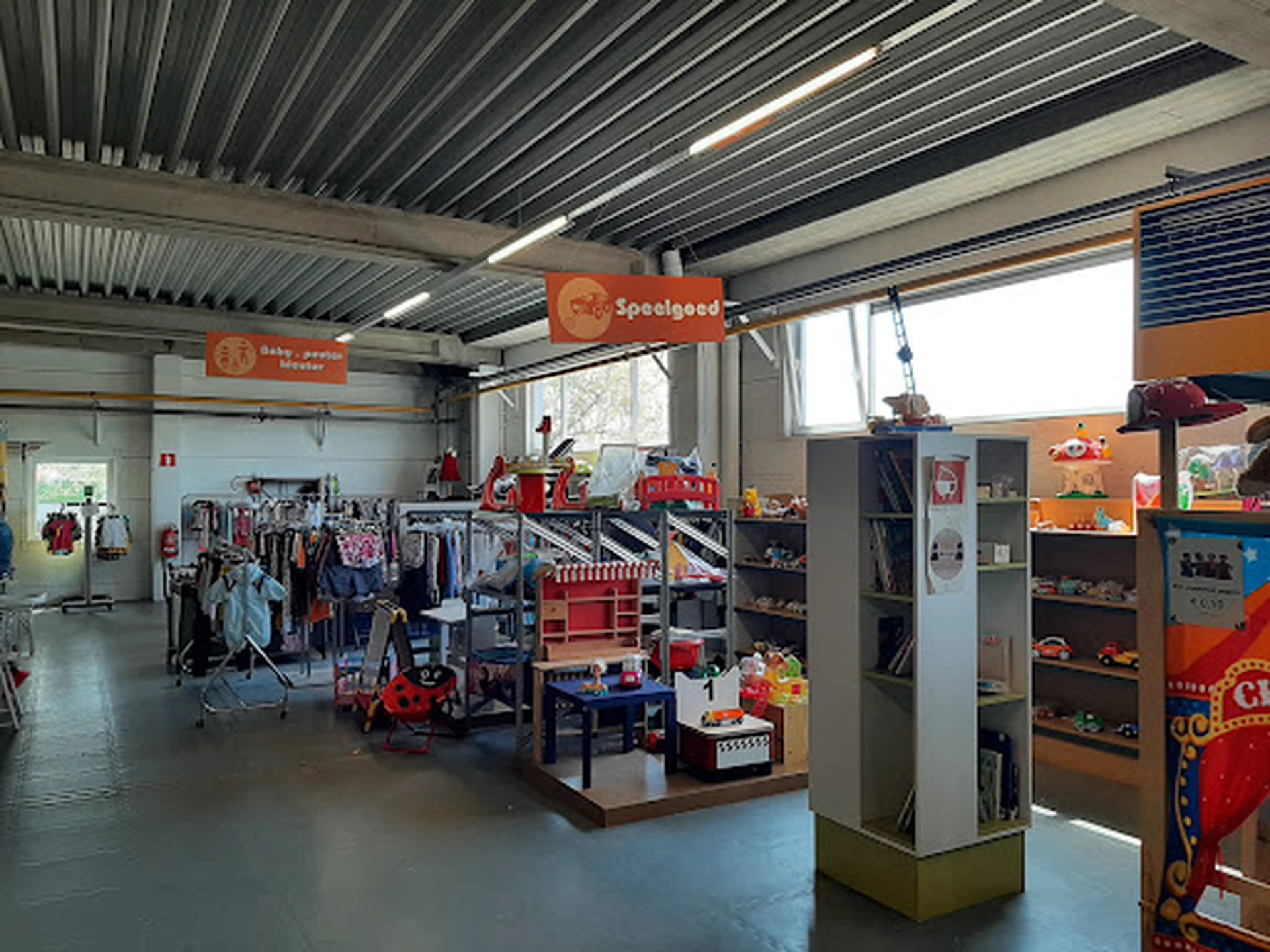 Winkelvloer met speelgoedrekken, displays en orange Sossigaad-signage onder golfplaten dak